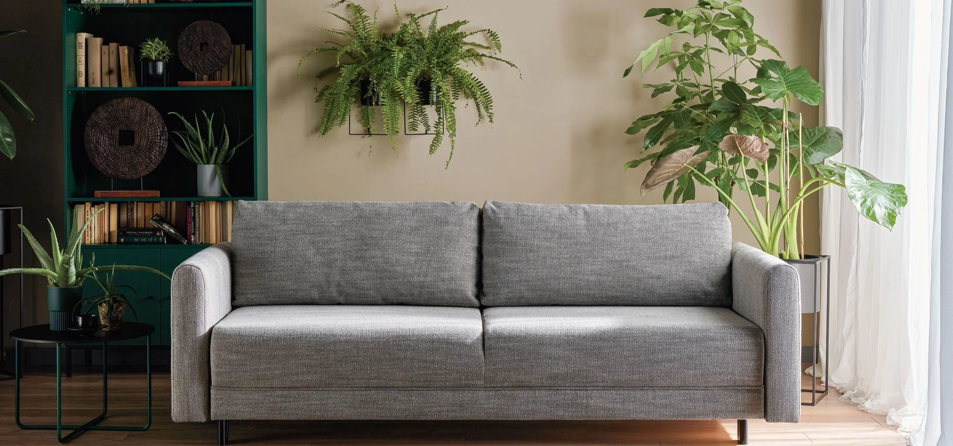 szara sofa w salonie otoczona roślinami doniczkowymi